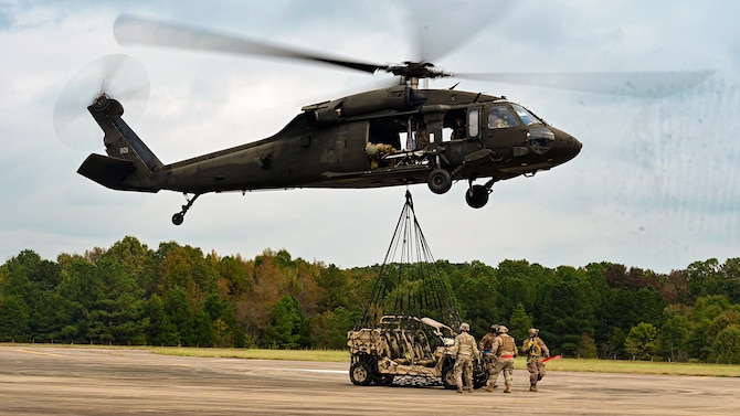 An off-road vehicle is attached to a helicopter for transport.