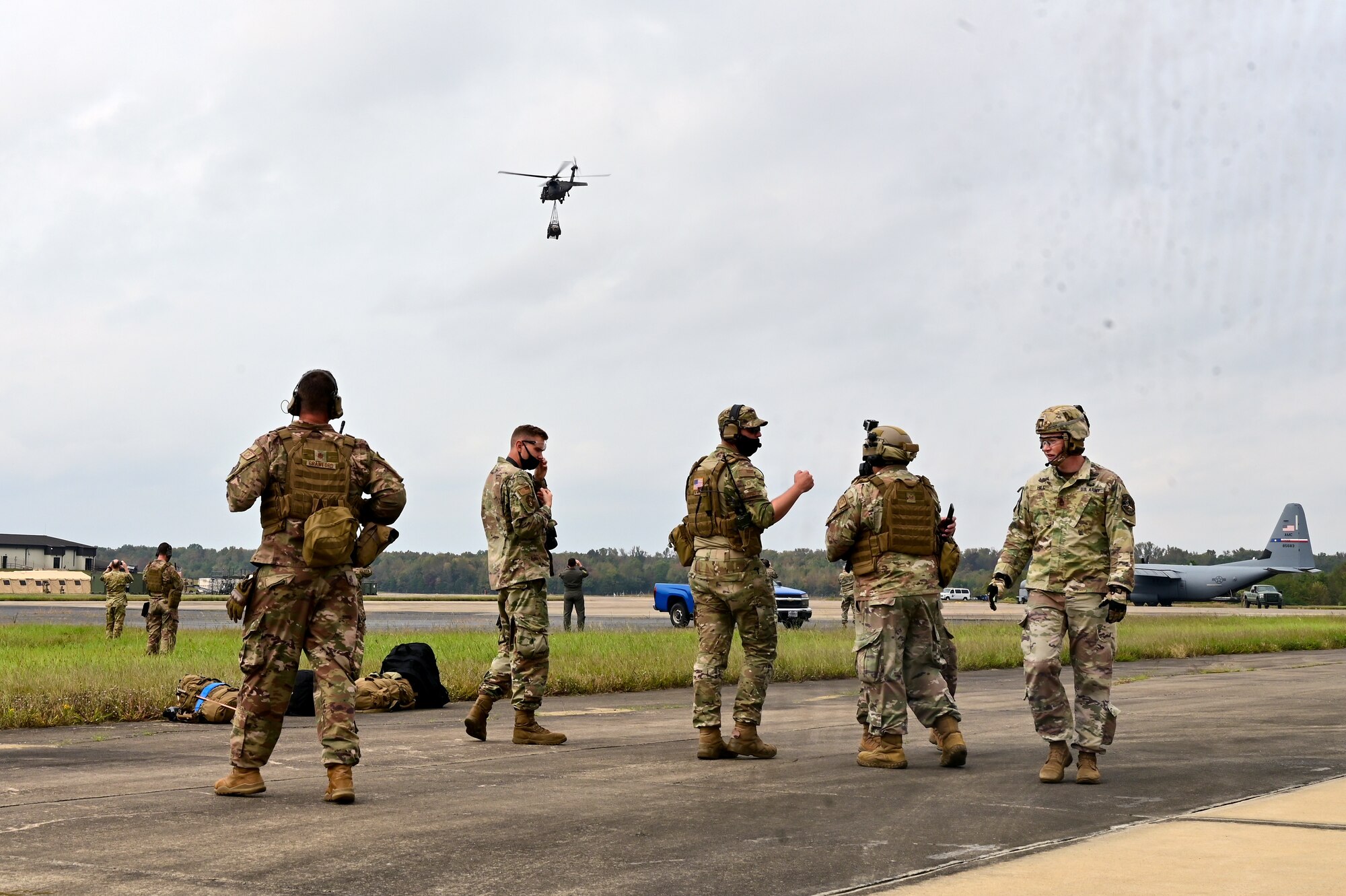A group of Airmen and Soldiers watch a helicopter fly away.