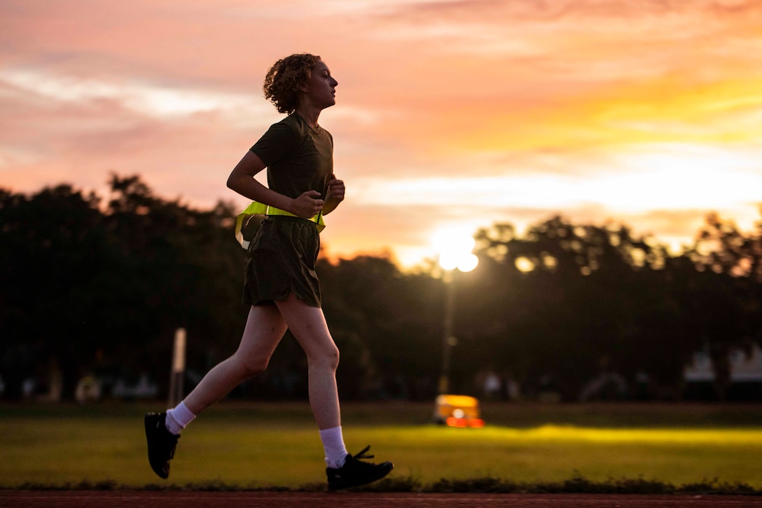 A Marine Corps recruit runs as the sun rises in the background.