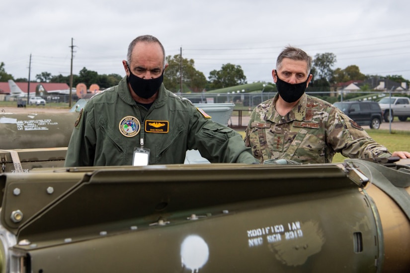 Two military leaders look at munitions at a military base.