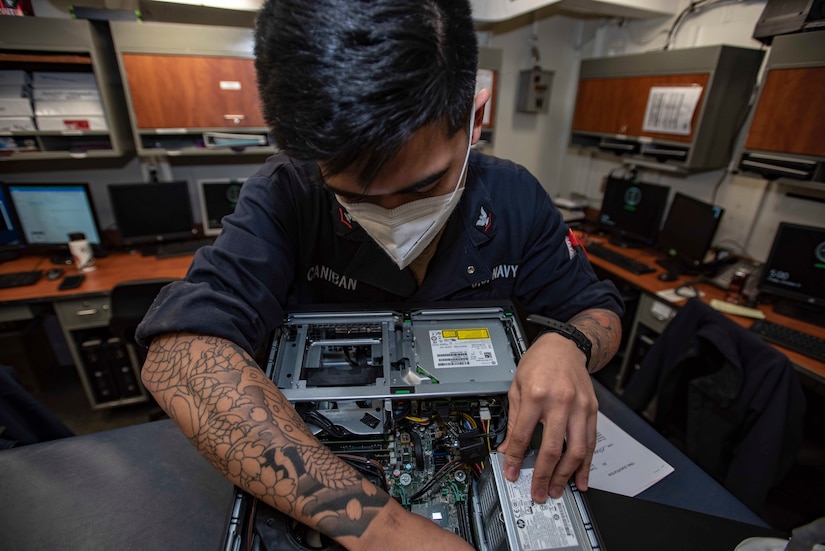 A sailor does maintenance on a computer.