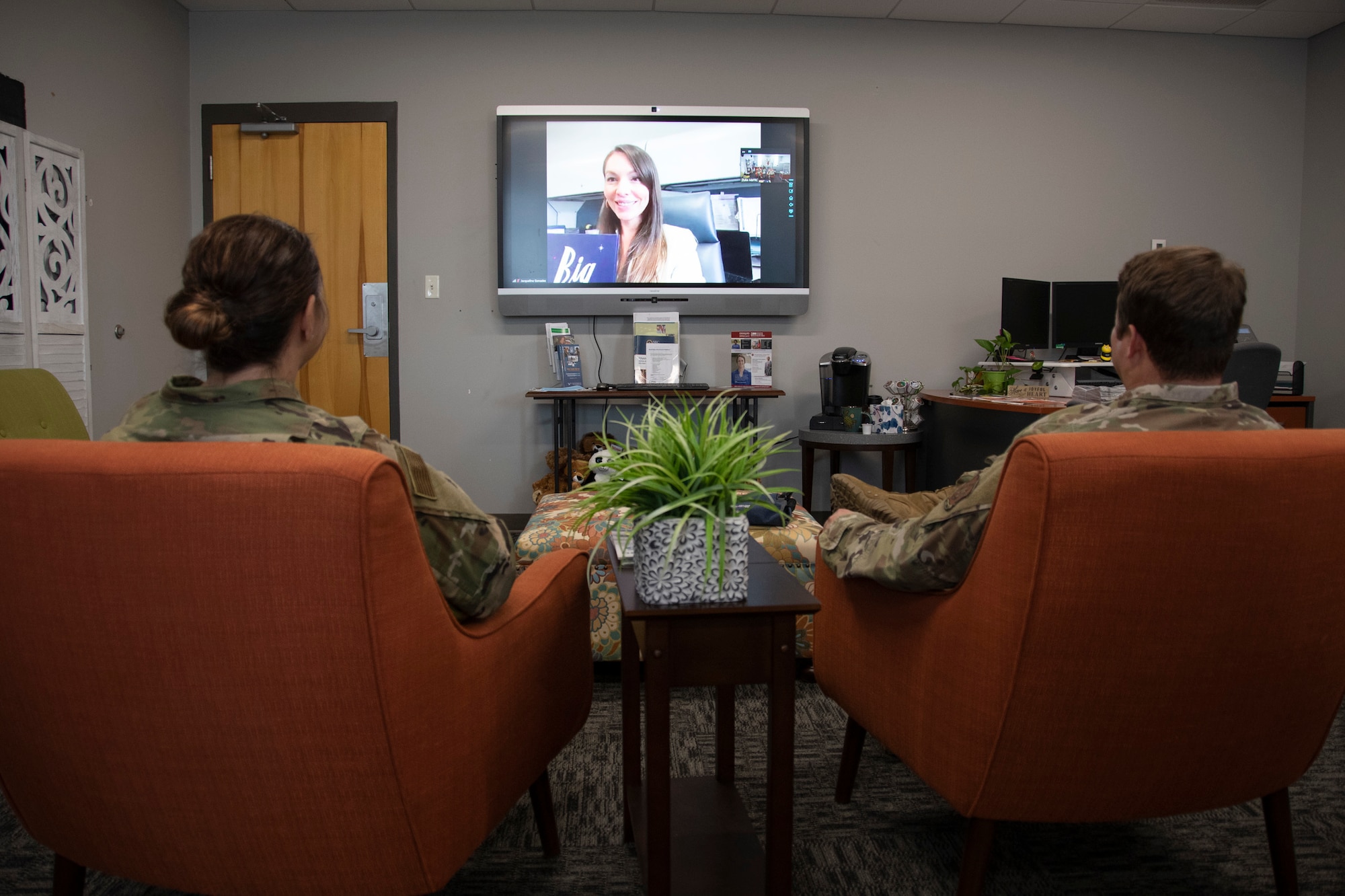 Photo of the back of two Airmen watching a TV