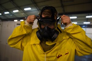 Photo of an Airman adjusting the straps of his gas mask