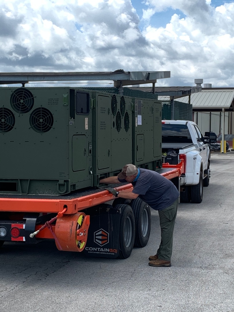 Man bent over looking over an electrical generator on a flatbed truck