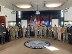 A group of military and civilian workers stand in a conference room.