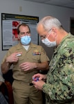 Lt. Cmdr. Sean Stuart, left, senior medical officer of the Emergency Department and director of the Combat Trauma Research Group (CTRG) at Naval Medical Center Portsmouth (NMCP), presents the iTClamp and other projects to Rear Adm. Bruce Gillingham, surgeon general of the U.S. Navy and chief of the Bureau of Medicine and Surgery, during his visit of NMCP on Oct. 21.