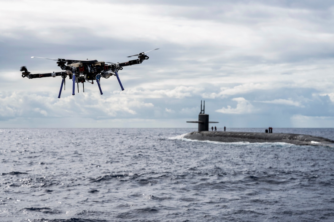 A drone flies over water near a submarine.