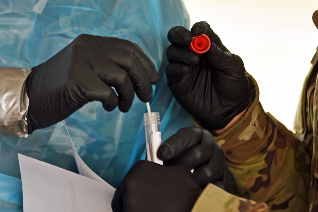 Two pairs of gloved hands place a nasal swab into a testing tube.