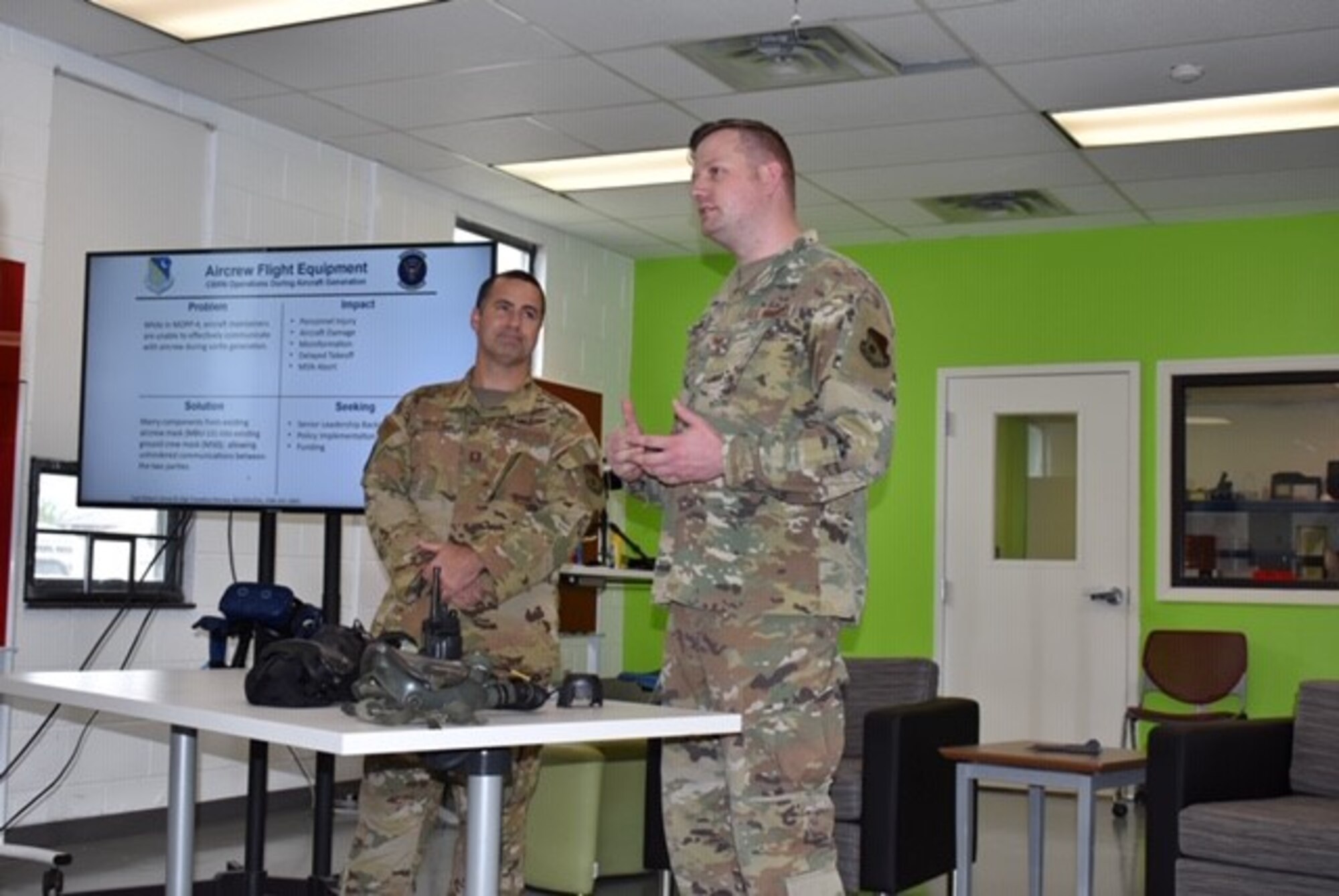 Photo shows two Airmen standing while addressing a room.