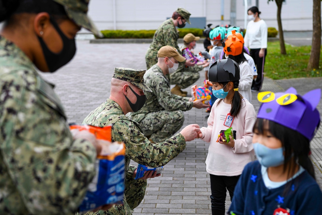 Sailors hand out candy to young students.