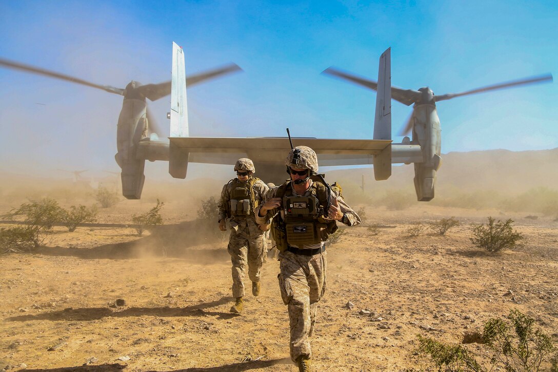 Two Marines exit an aircraft in a desert-like area.