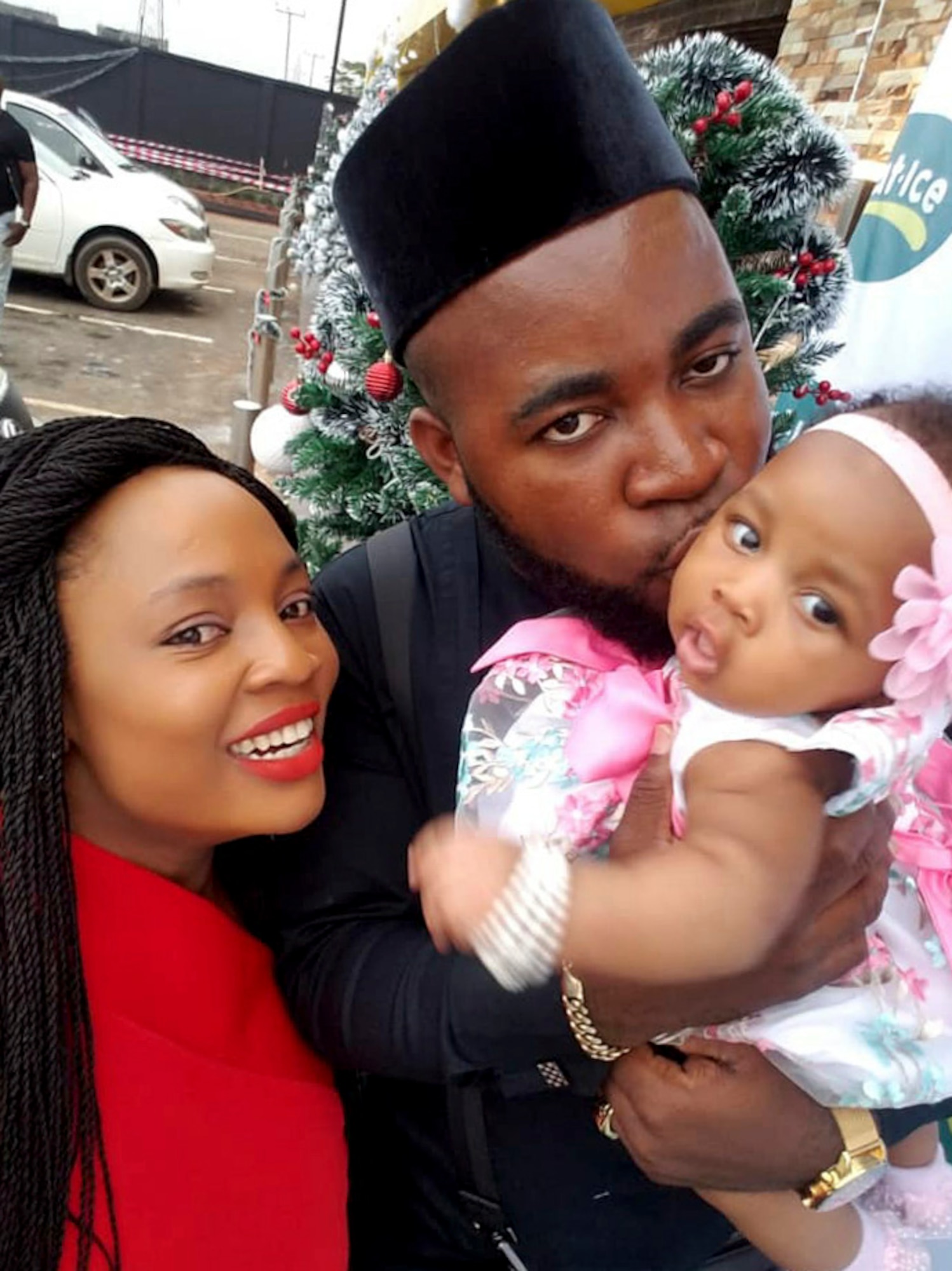 A mother smiles as father holds an infant and kisses it.