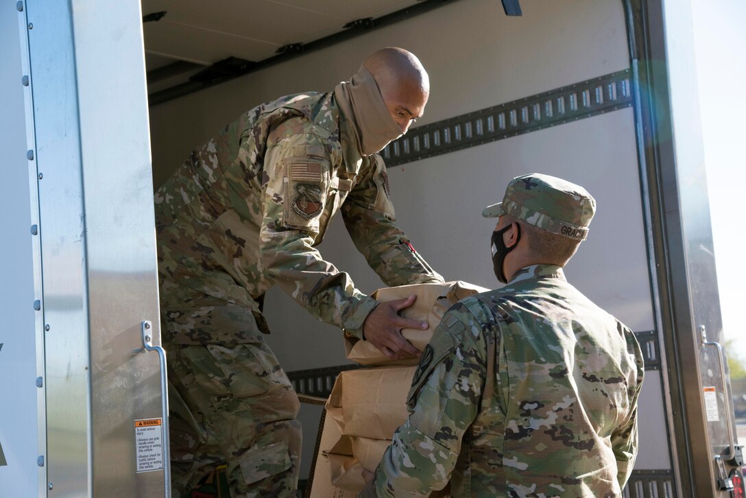 Two guardsmen unload boxes of food from a truck.