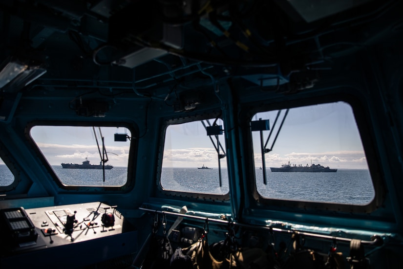 Three ships can be seen from the windows on the bridge of a fourth ship.