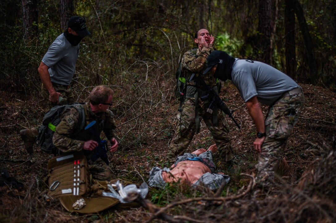 Special Operations Surgical Team candidates participate in a medical scenario providing emergency medical assistance to a subject on the leaf-covered ground in a woods