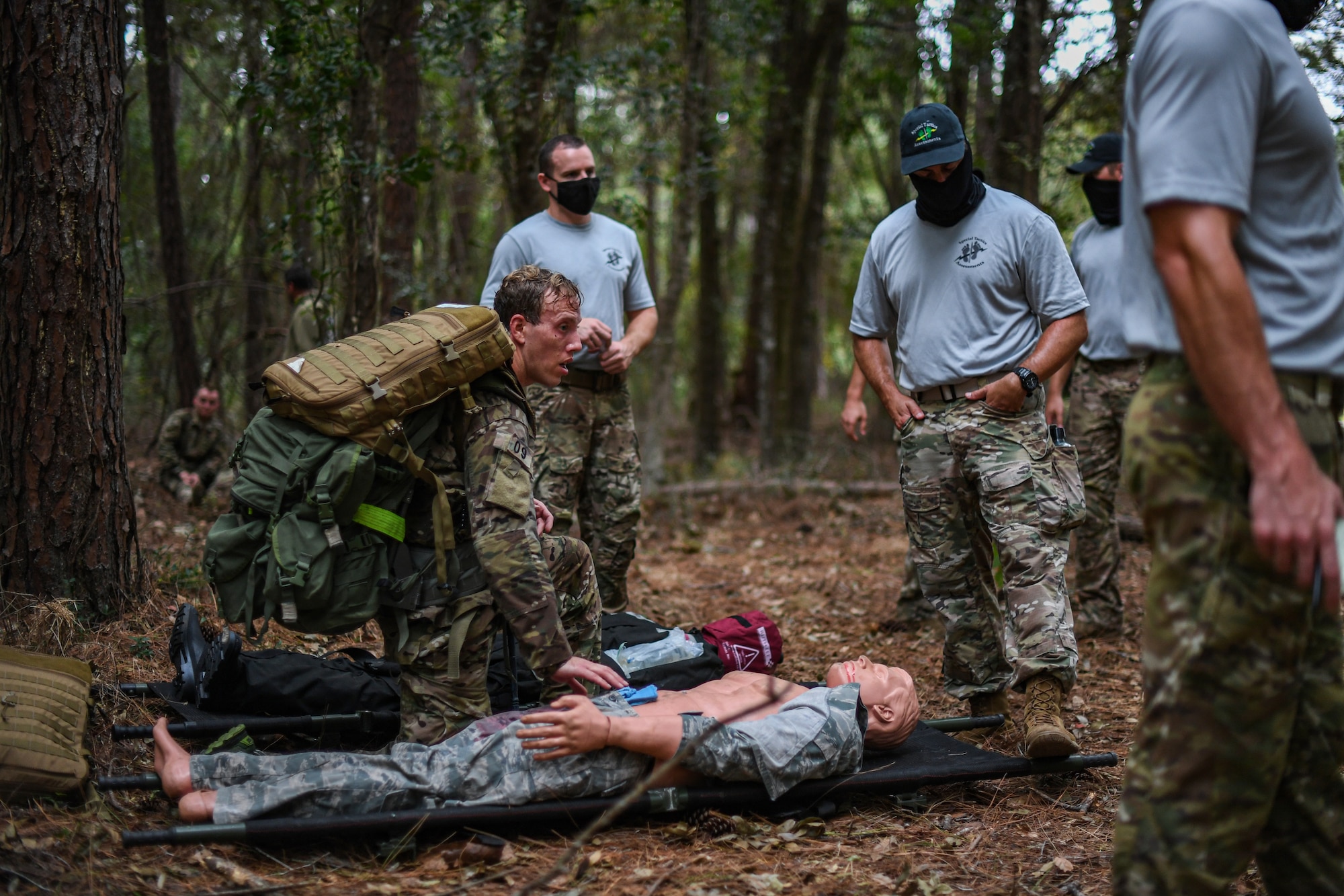 Special Operations Surgical Team candidates participate in a medical scenario providing emergency medical assistance to a subject on the leaf-covered ground in a woods