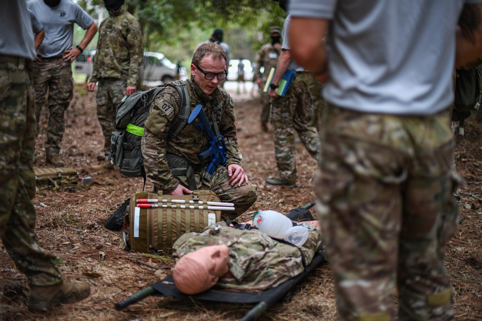 Special Operations Surgical Team candidates participate in a medical scenario providing emergency medical assistance to a subject on the leaf-covered ground in a woods
