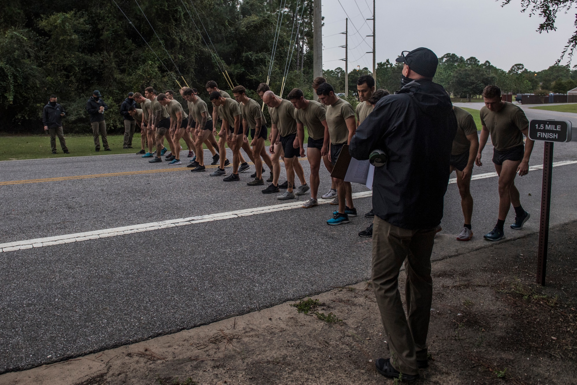 Special Tactics tactical air control party candidates are lined up in a row across a road at the start of a running test. They lean forward ready for the start.
