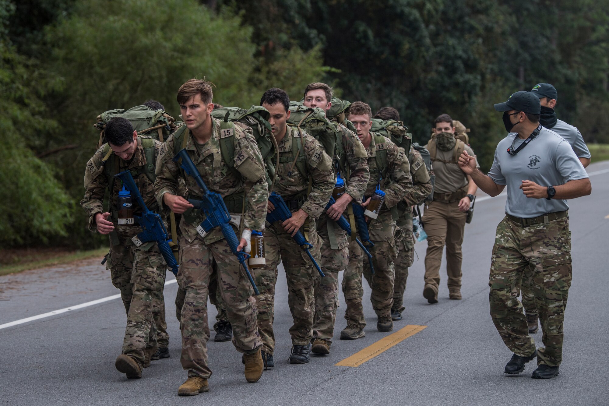 A team of two rows of five Special Tactics tactical air control party candidates carry heavy packs and weapons while cadre motivates the candidates