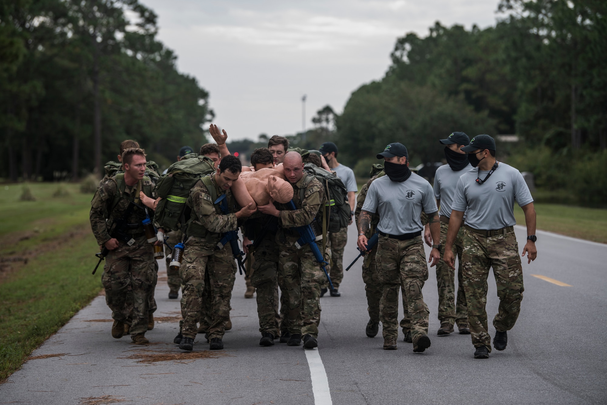 A small group of Special Tactics tactical air control party candidates carry a mannequin between them using just their arms while walking beside a road during an assessment