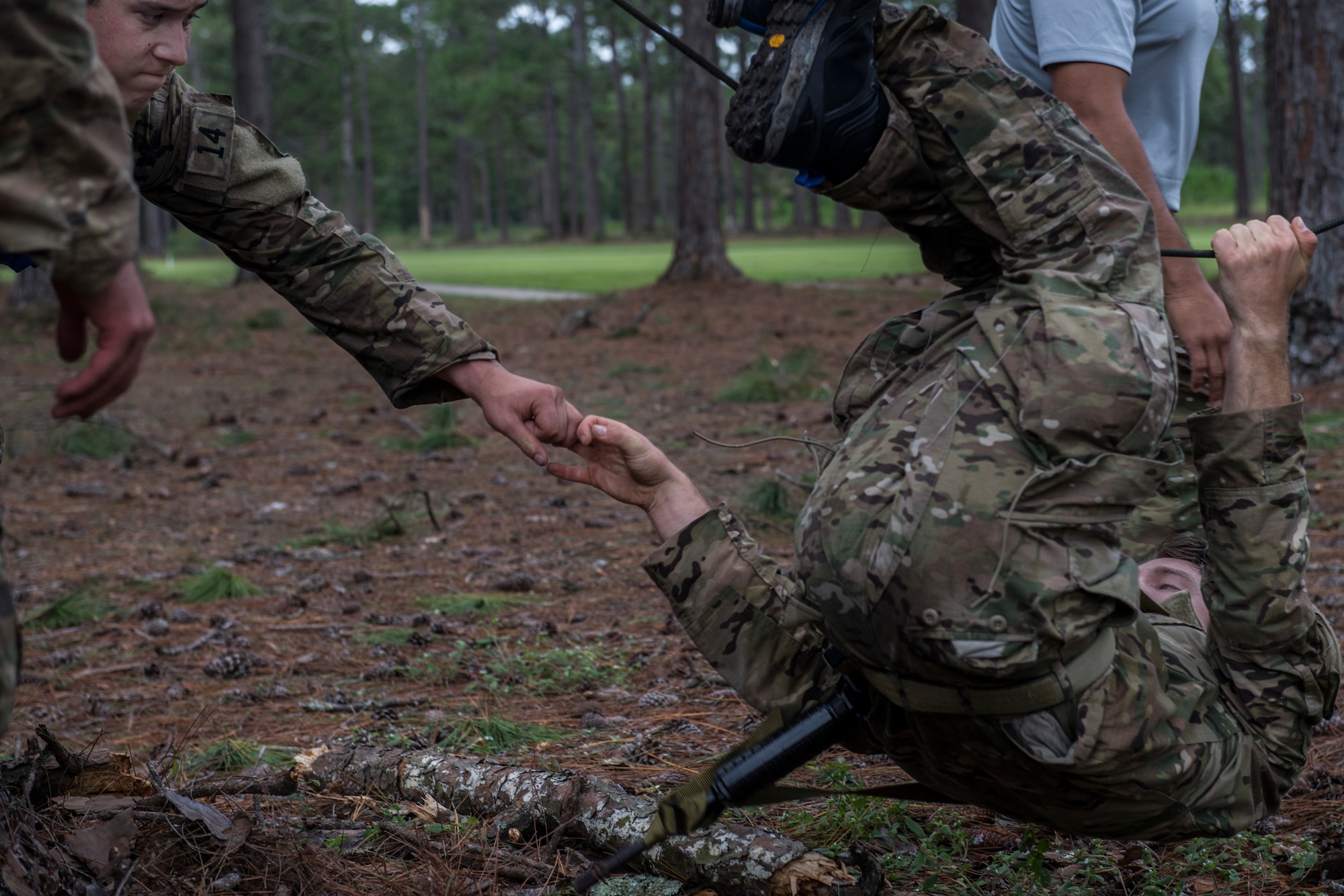 A Special Tactics tactical air control party candidate lies in the mud with his legs in the air while another candidate leans into the picture to grasp his hand.