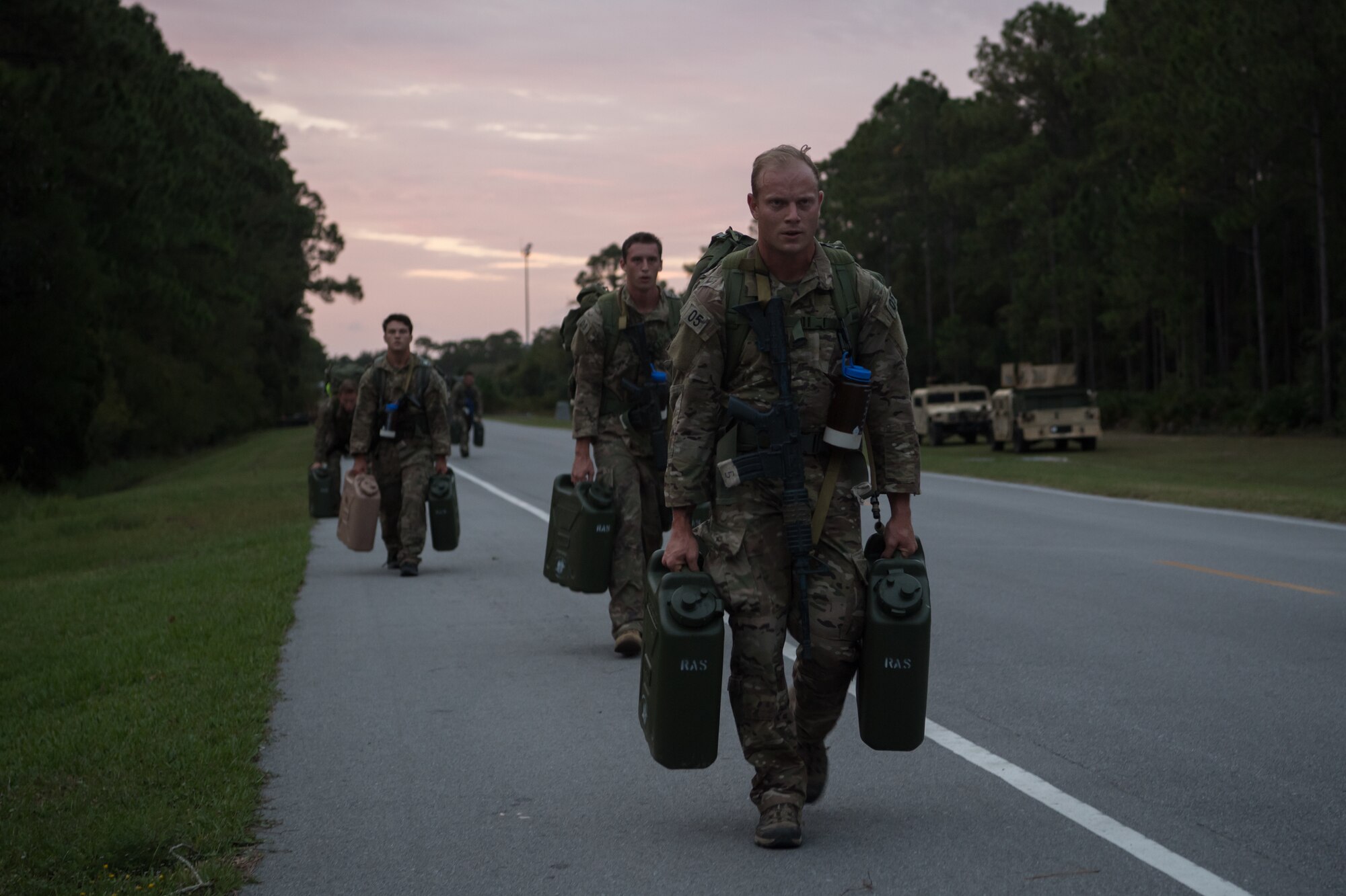 A line of Special Tactics tactical air control party candidates walk toward us carrying pairs of jerry cans along the side of a road.