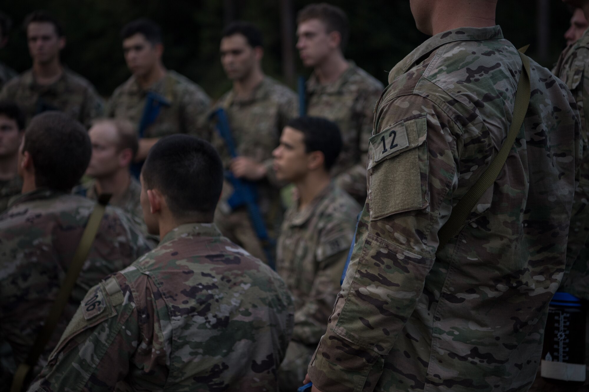 Special Tactics tactical air control party candidates stand in a group around a cadre member listening to feedback regarding a portion of their assessment.