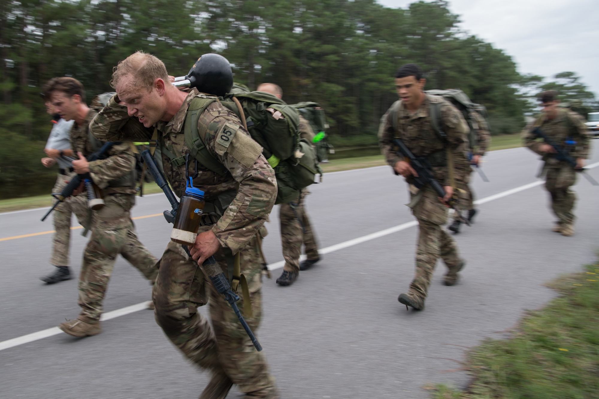 Special Tactics tactical air control party candidates quickly walk down a road carrying heavy ruck sacks with their team