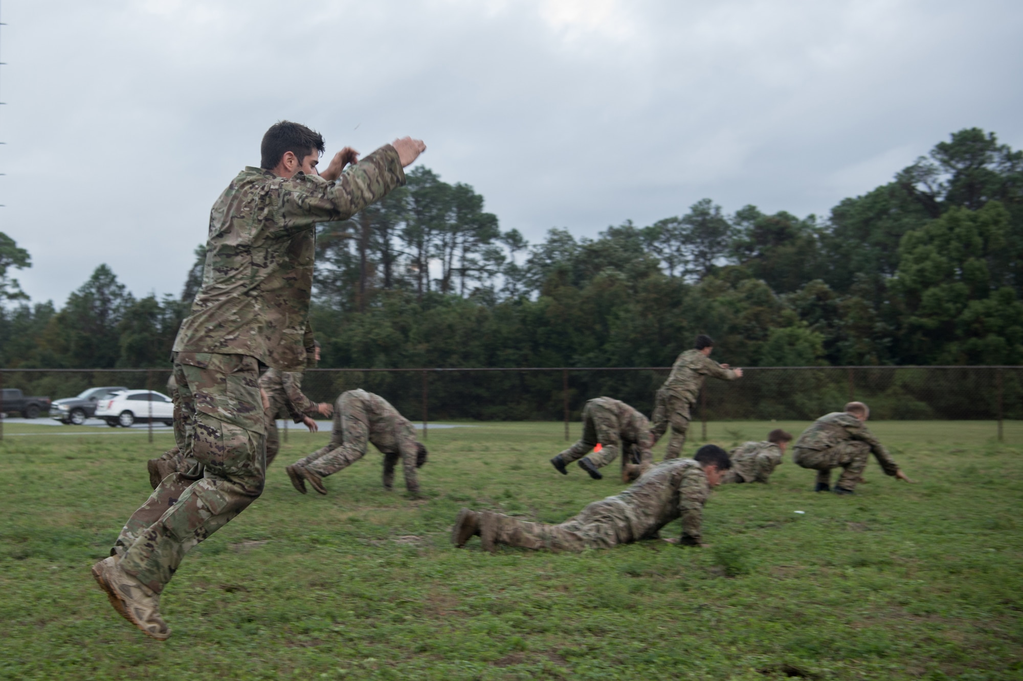 We have a side view of Special Tactics Tactical Air Control Party candidates conducting "Flying Burpees." Some are rocking forward on the ground while others are jumping into the air.