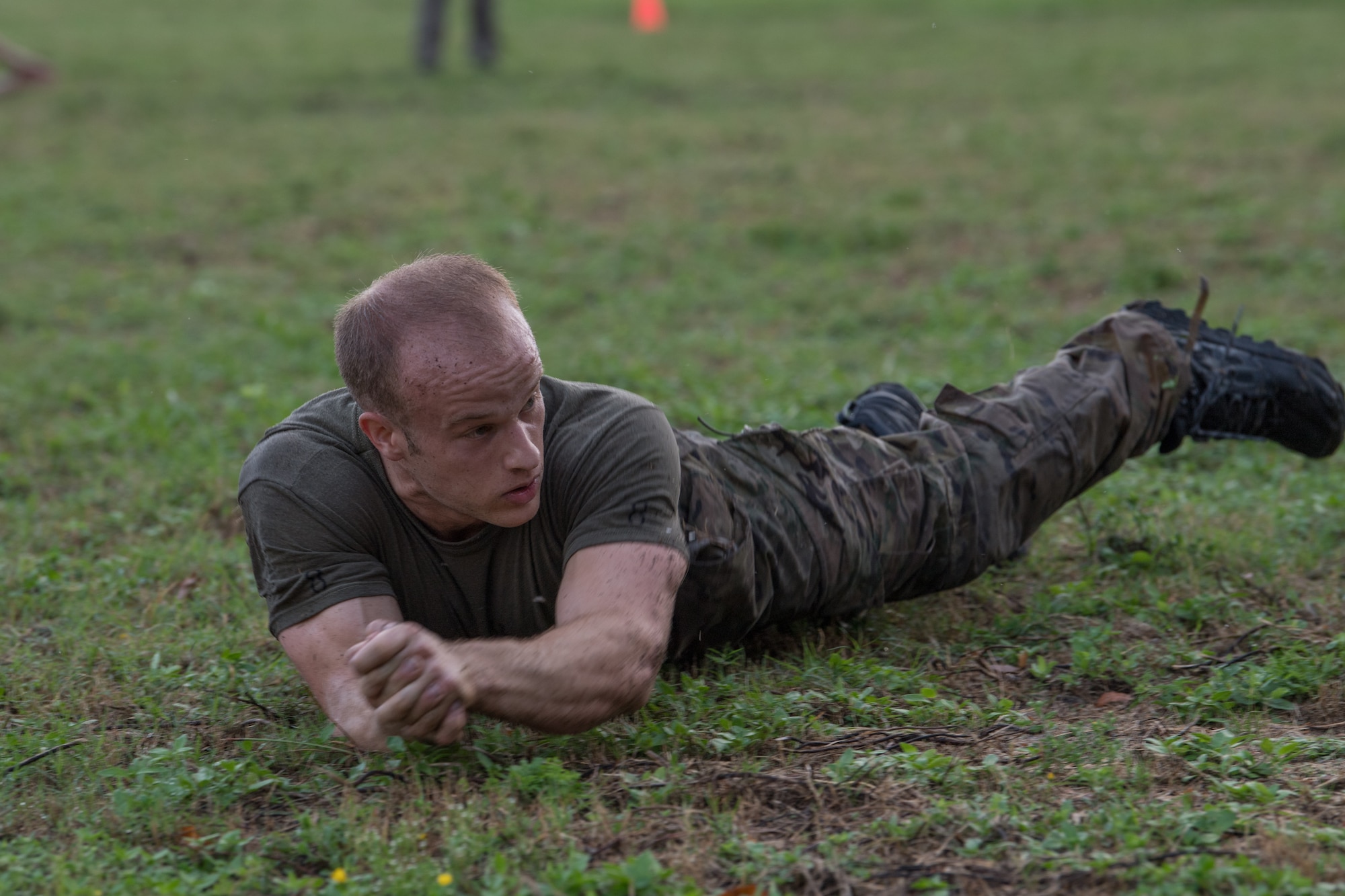 A Special Tactics tactical air control party candidate log rolls across a field by rolling from his back to his side to his front to his side on a wet day.