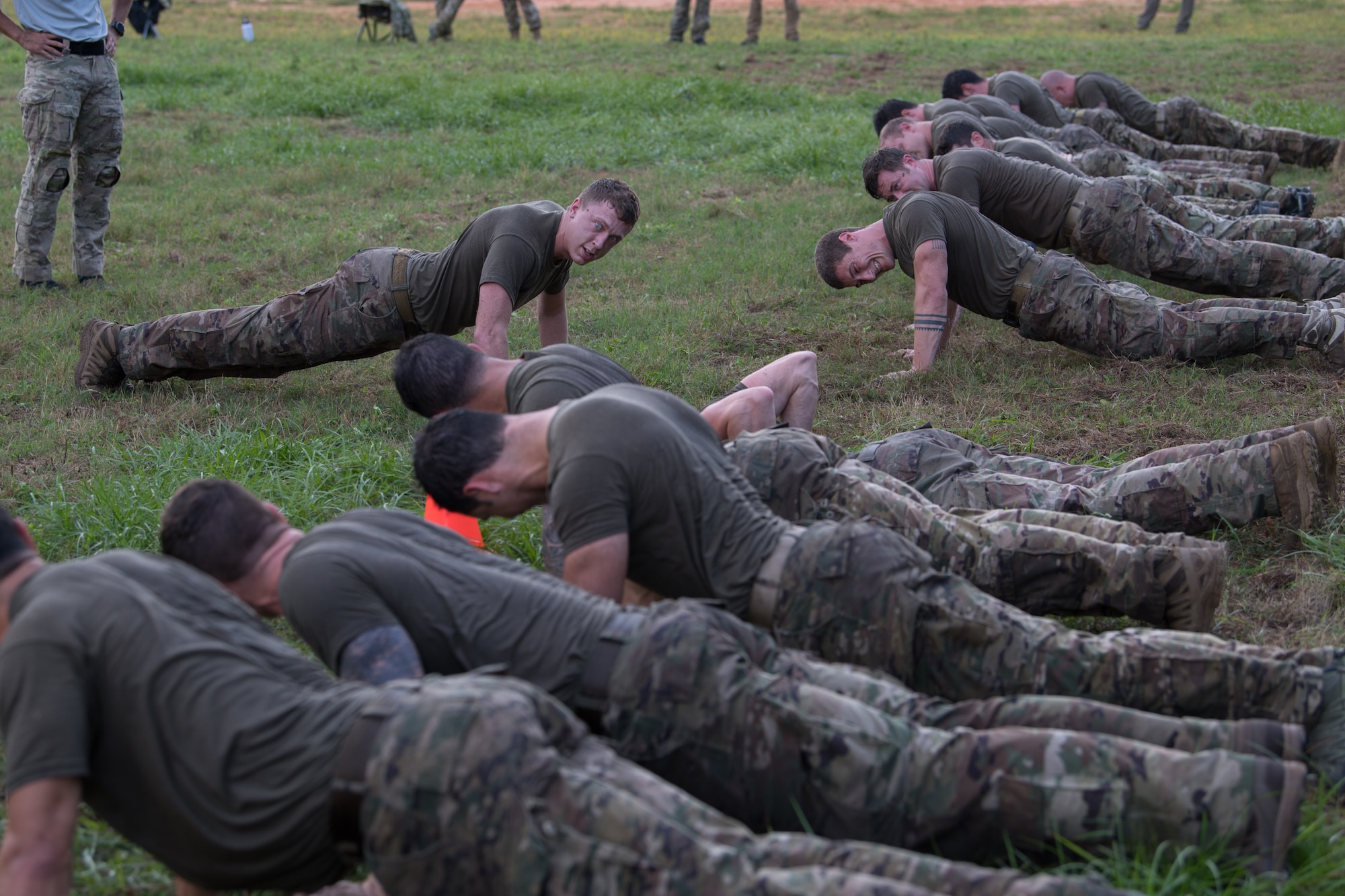 A Special Tactics tactical air control party candidate leads his teammates in pushups during assessment, a single Airman facing rows of other candidates.