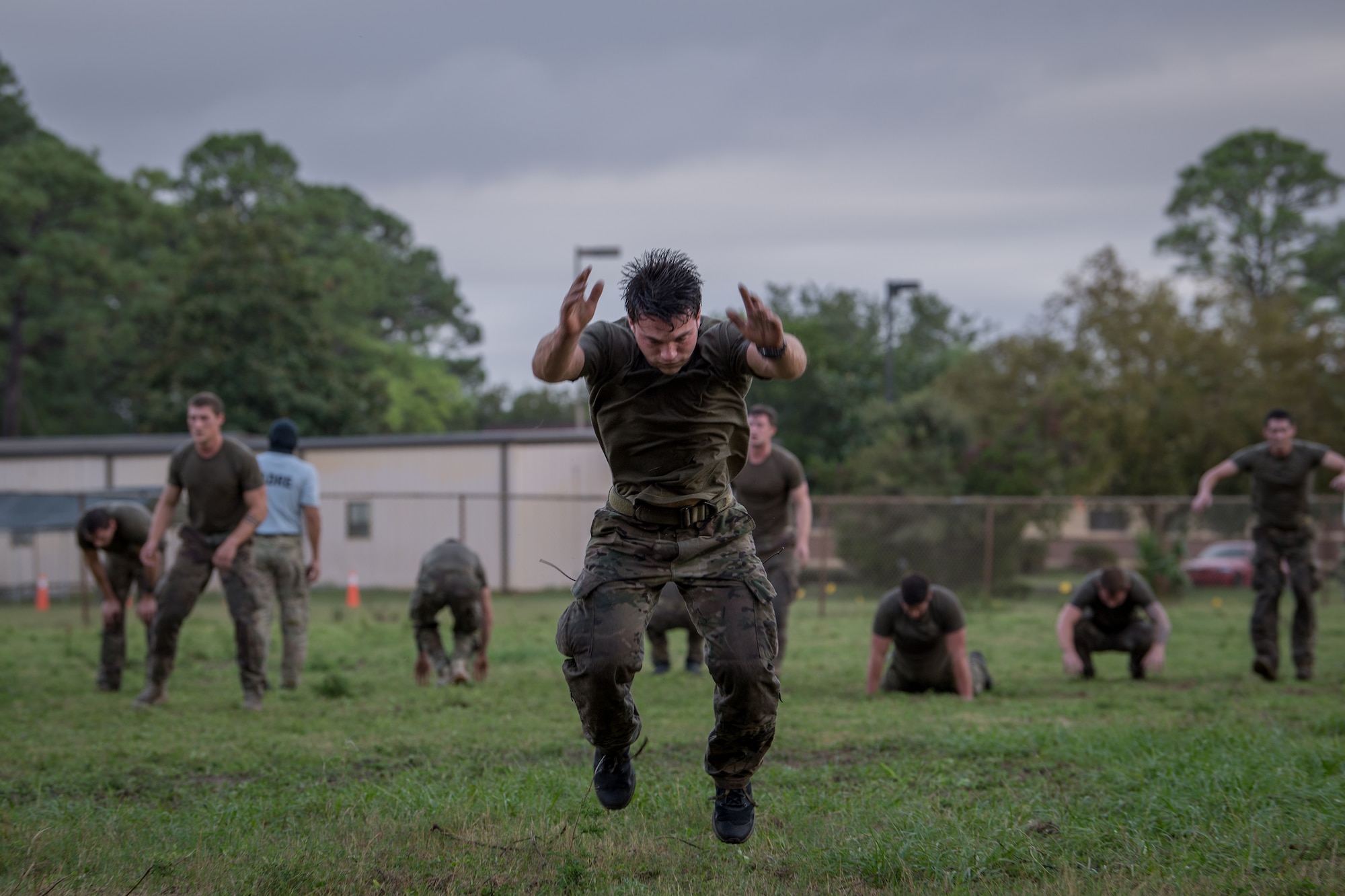 A Special Tactics tactical air control party candidate participates in leaping burpees during their assessment. Several airmen are caught in mid-flight by the picture.