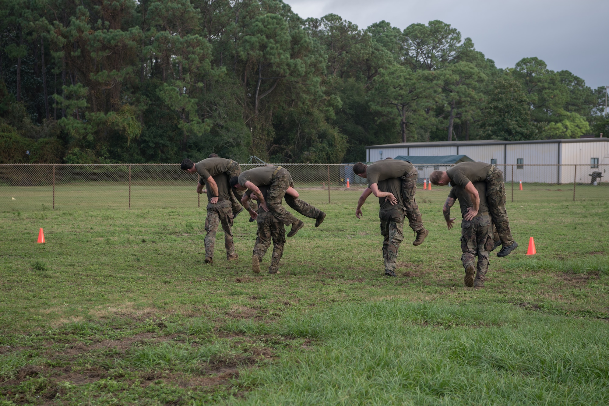 Four Special Tactics tactical air control party candidates carry teammates across a grass field during their assessment.