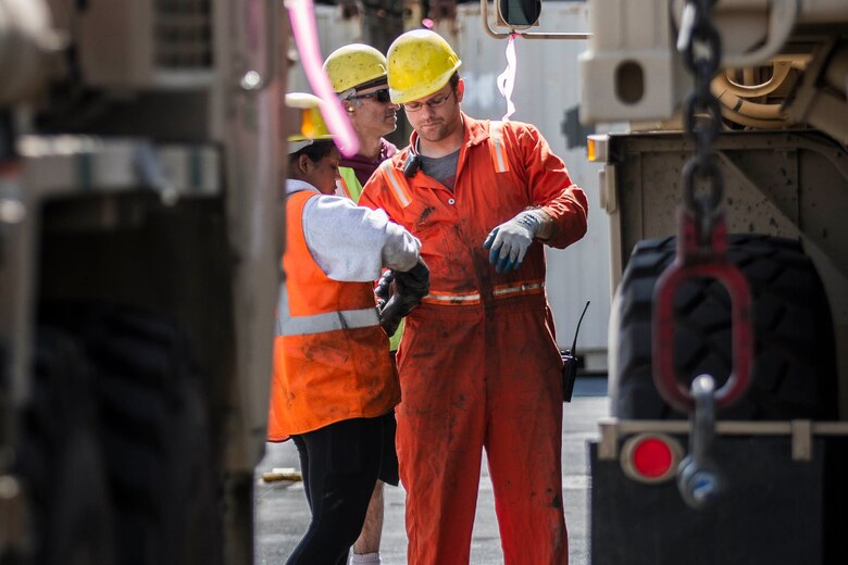 People in hard hats stand between large trucks.