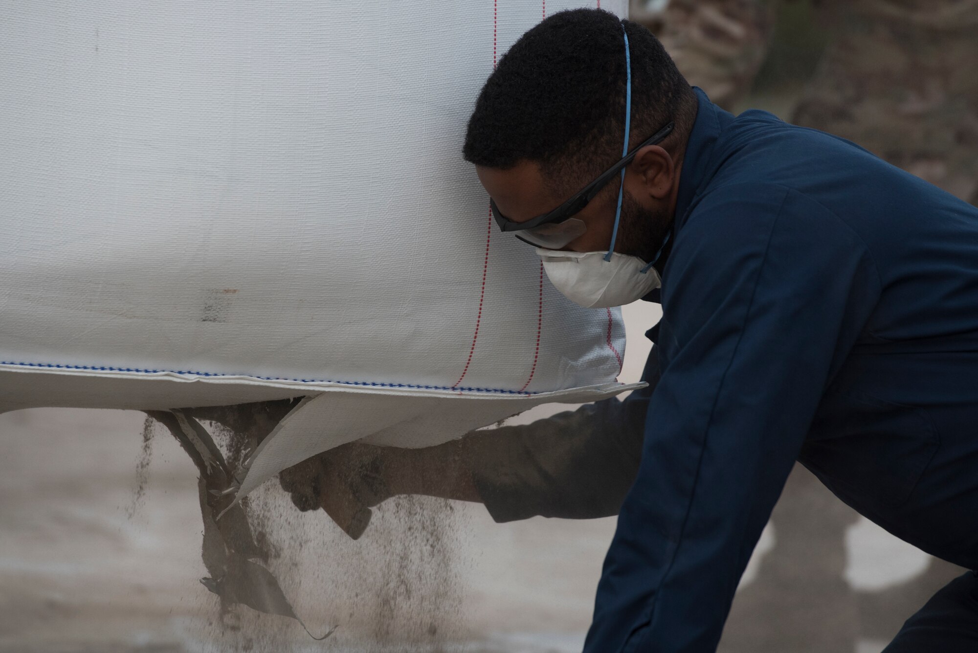 An Airman cuts the bottom of a cement bag.