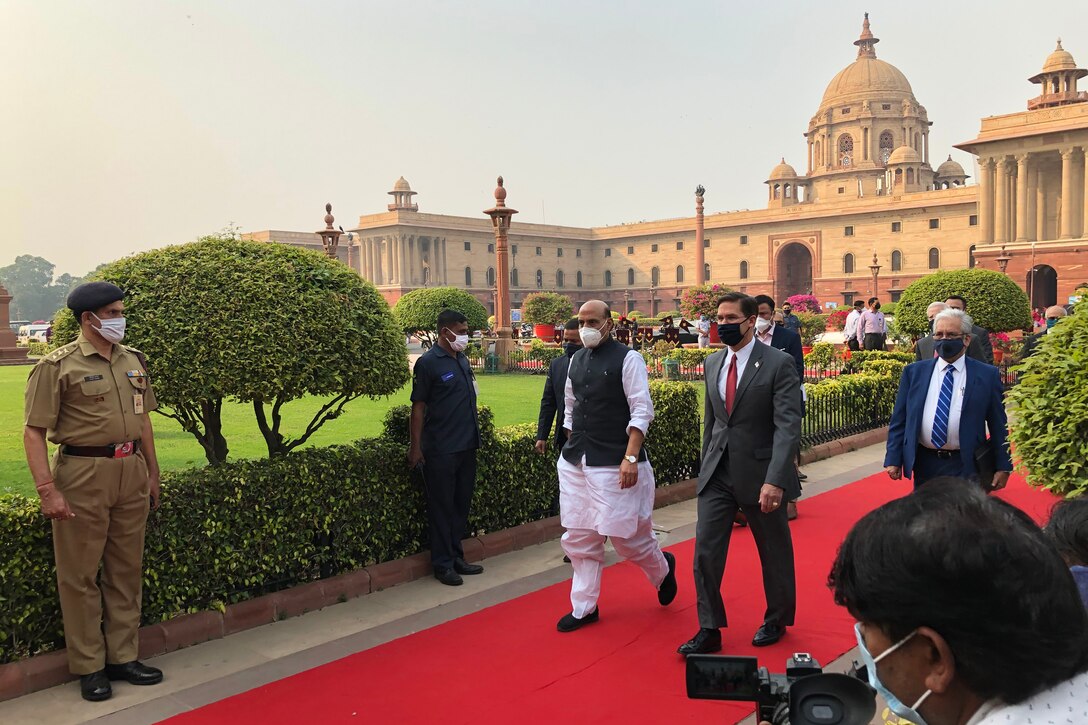 Two men walk on a red carpet while others stand at attention.