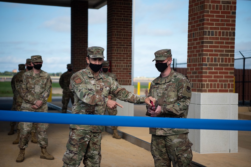 An Airman hands another Airman a giant pair of scissors to cut a ribbon to open a new government vehicle fuels facility.