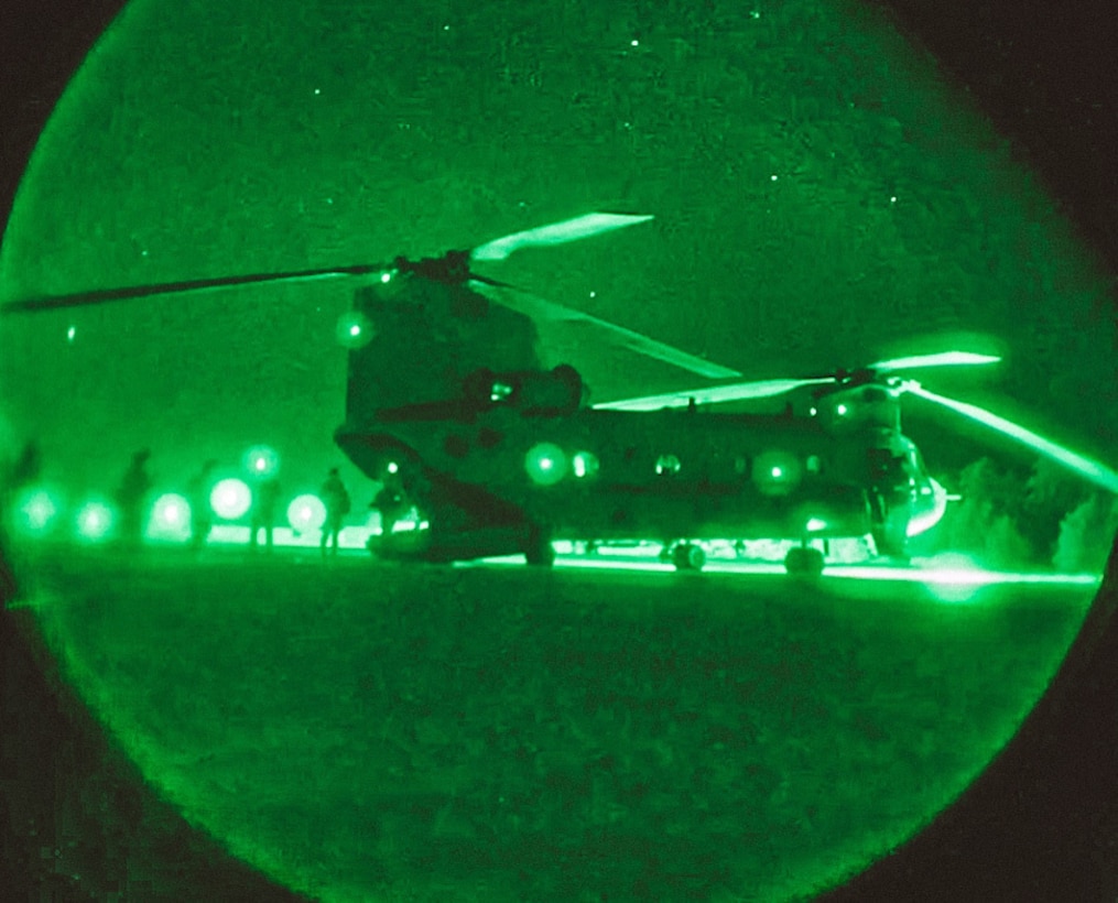 Soldiers load into a helicopter at night illuminated by green light.