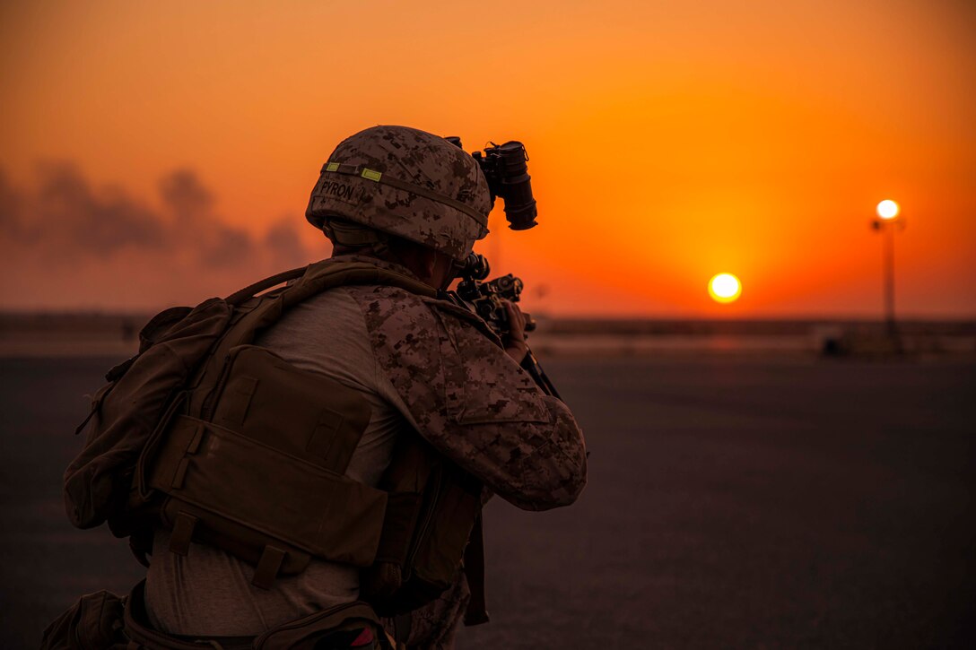 A Marine points his weapon as the sun sets in the distance.