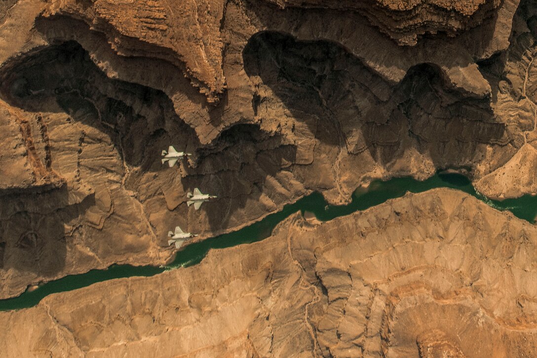 Three aircraft, shown from above, fly over a section of the Grand Canyon bisected by a thin green river.