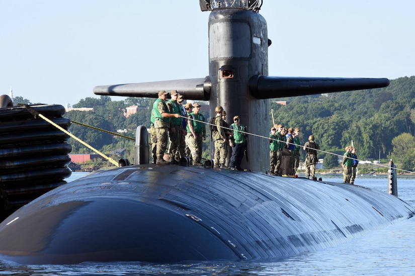 Sailors stand on top of a submarine while one of them holds a line.