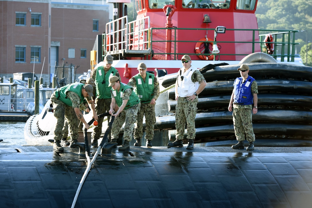 Sailors stand on top of a submarine while two of them hold a looped line.