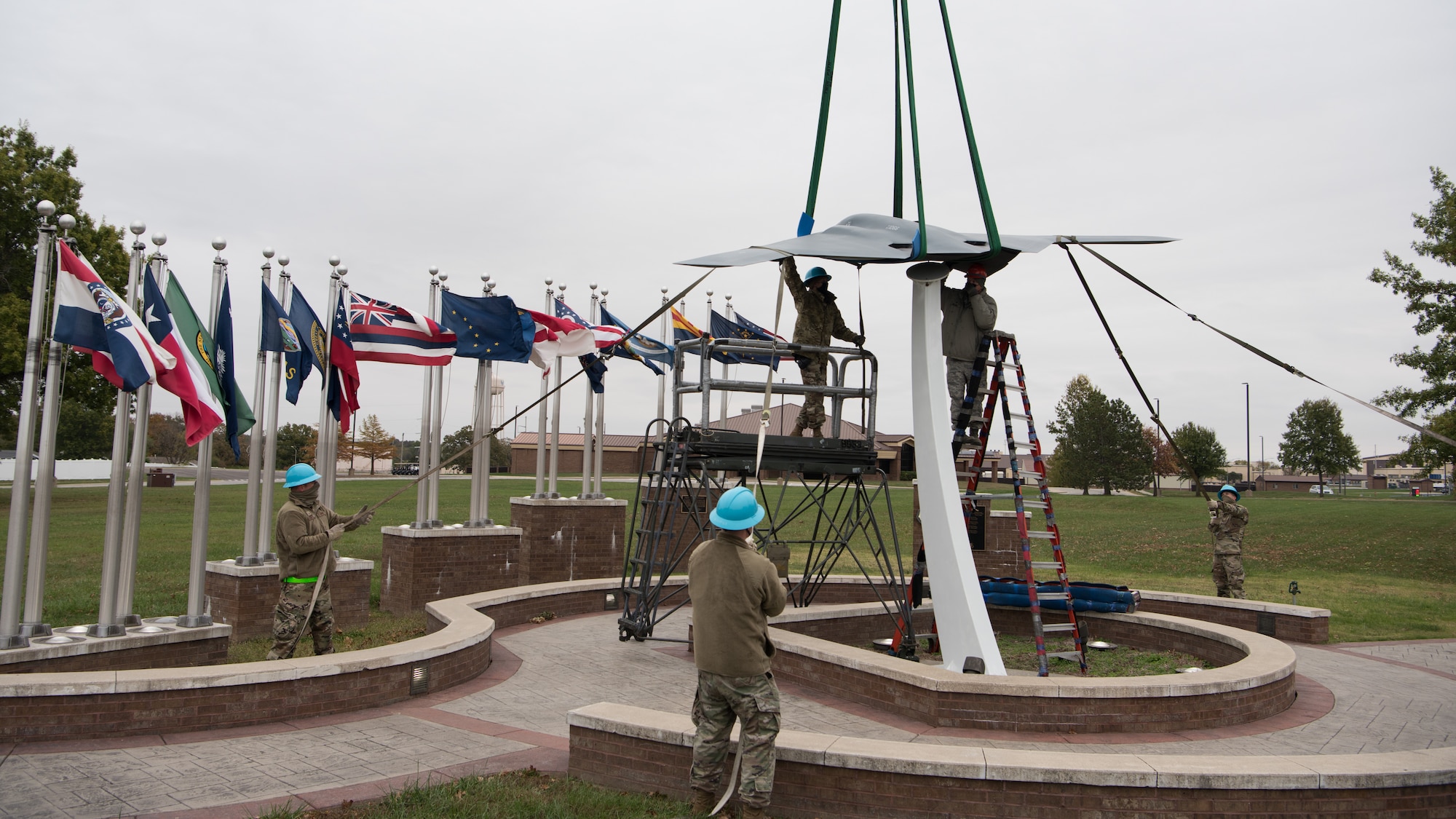 Airmen seat the B-2 static display on its pedestal in front of a set of flags.