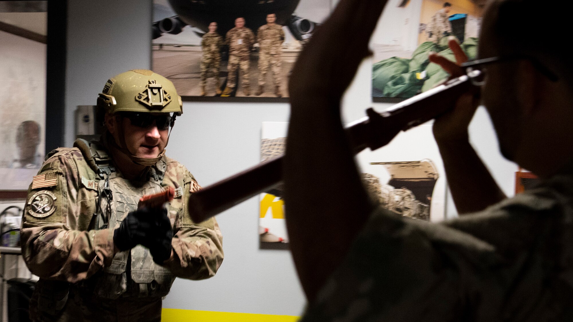 A security forces Airman in combat gear points a red training pistol at an armed suspect, the suspect has his arms raised in surrender.