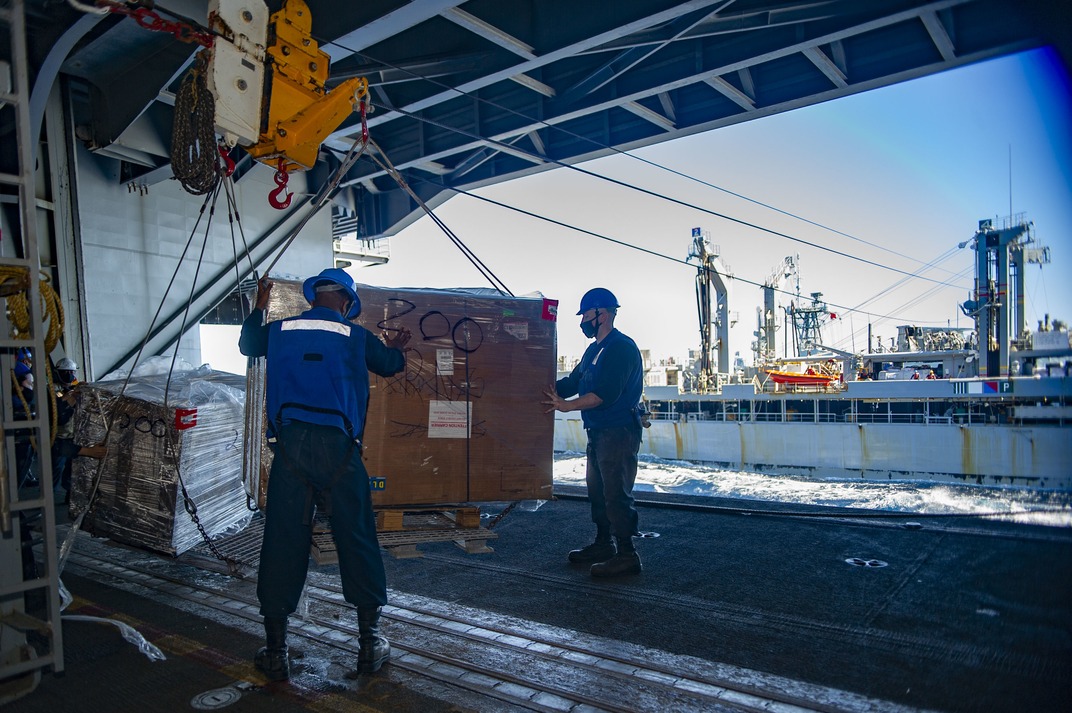 Boatswain's Mate Seaman Corey Howard, left, from Tampa, Fla., and Boatswain's Mate 3rd Class Corey Hester, from Kings Mountain, N.C., receive supplies in the hangar bay of the Navy's only forward-deployed aircraft carrier USS Ronald Reagan (CVN 76) during a replenishment-at-sea with dry cargo and ammunition ship USNS Tippecanoe (T-AO 199).