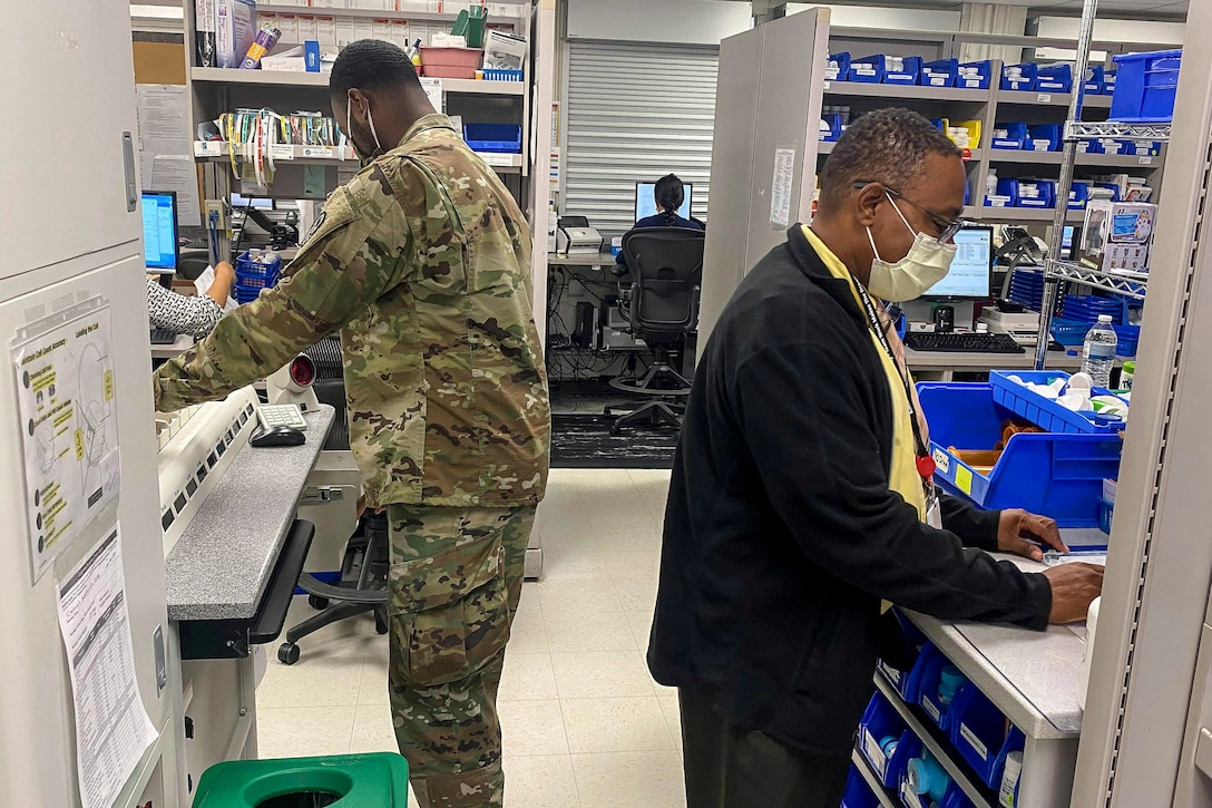 A service member and civilian work at pharmacy counters.
