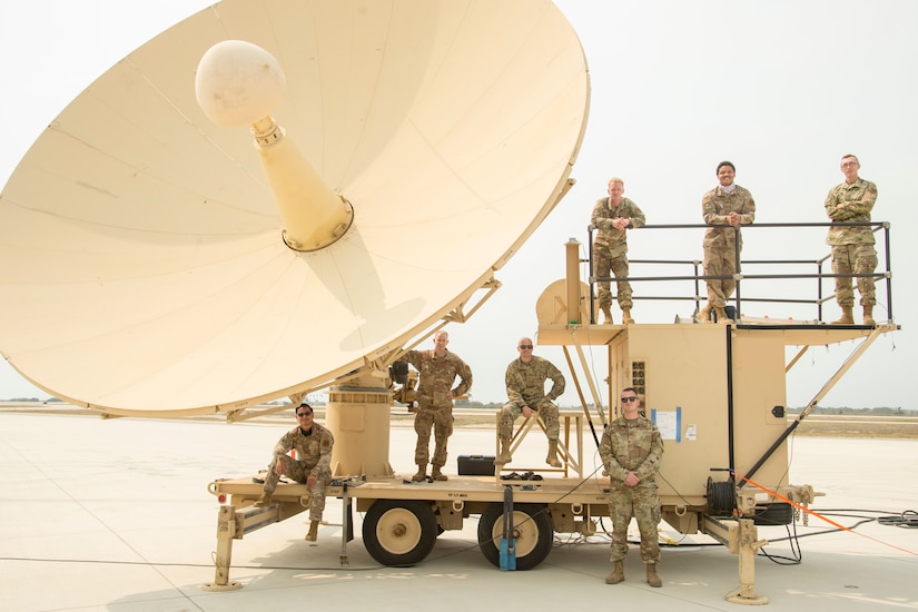 Airmen pose for a photo in front of a satellite terminal.