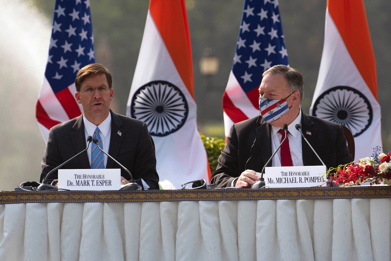 Defense Secretary Dr. Mark T. Esper sits and speaks at a table as Secretary of State Michael R. Pompeo looks on.