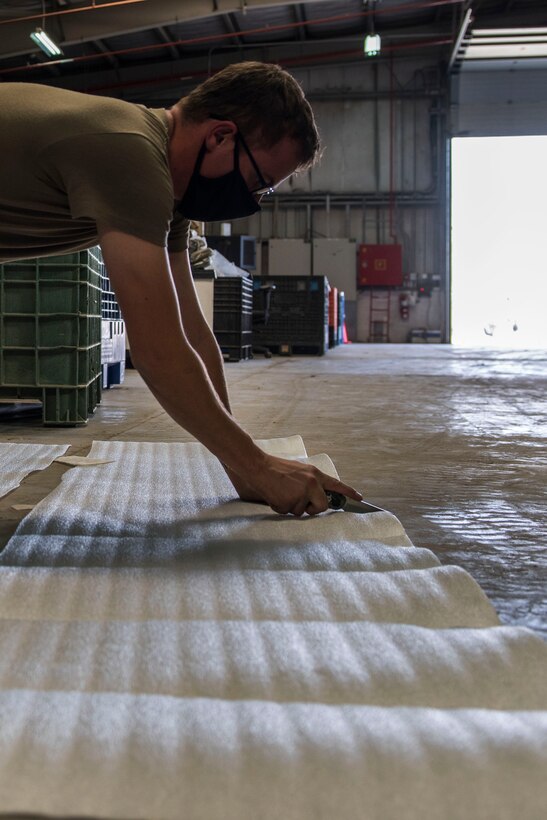 U.S. Air Force Airman 1st Class Bradan Phelps, 380th Expeditionary Logistics Readiness Squadron supply technician, cuts wrapping paper at the individual protective equipment (IPE) warehouse on Al Dhafra Air Base, United Arab Emirates, Oct. 27, 2020