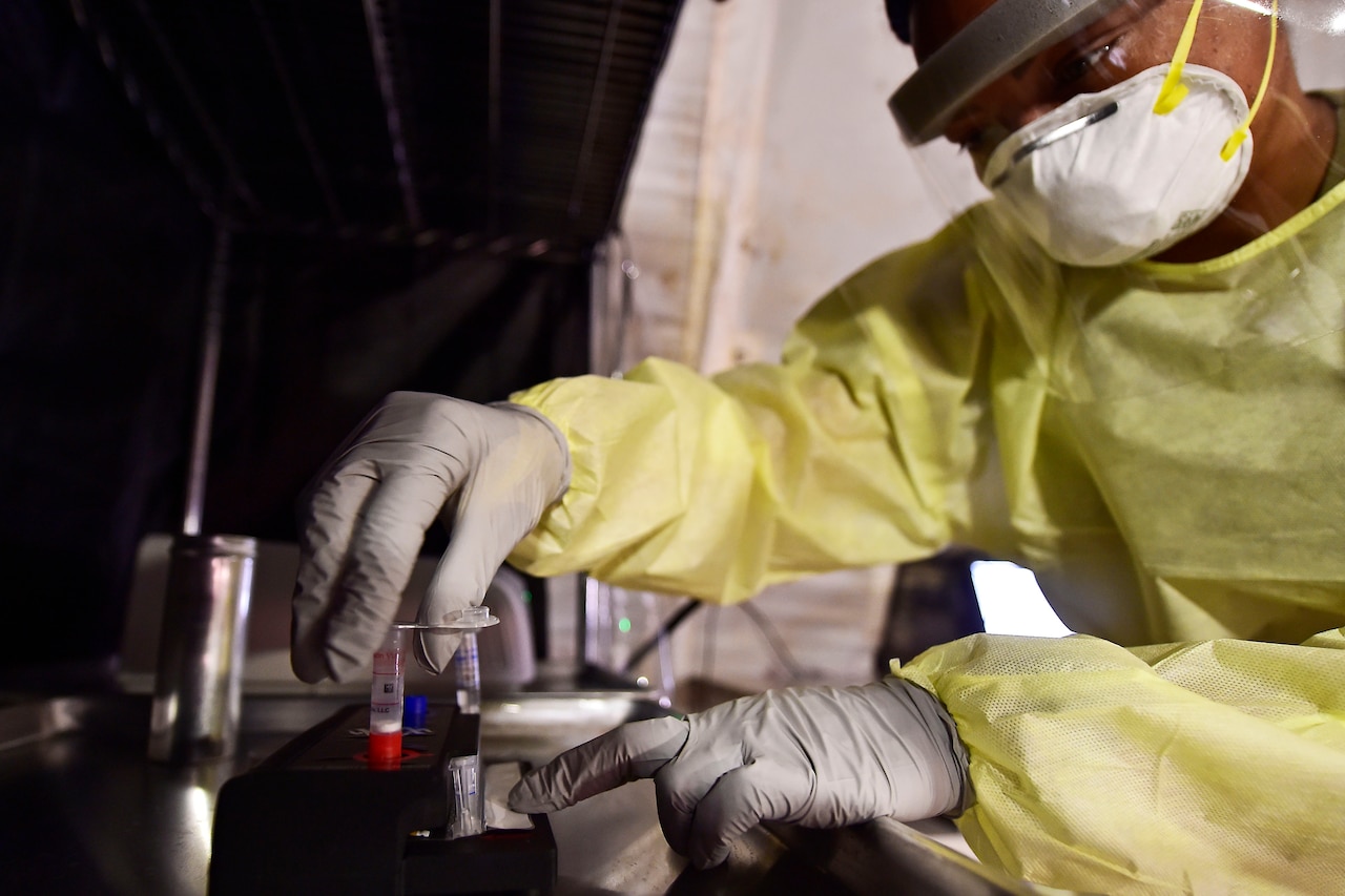 An airman wearing personal protective equipment installs test equipment.